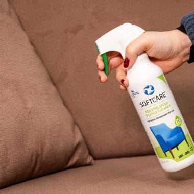 Person holding a textile cleaning product in front of the sofa