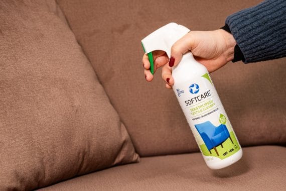 Person holding a textile cleaning product in front of the sofa