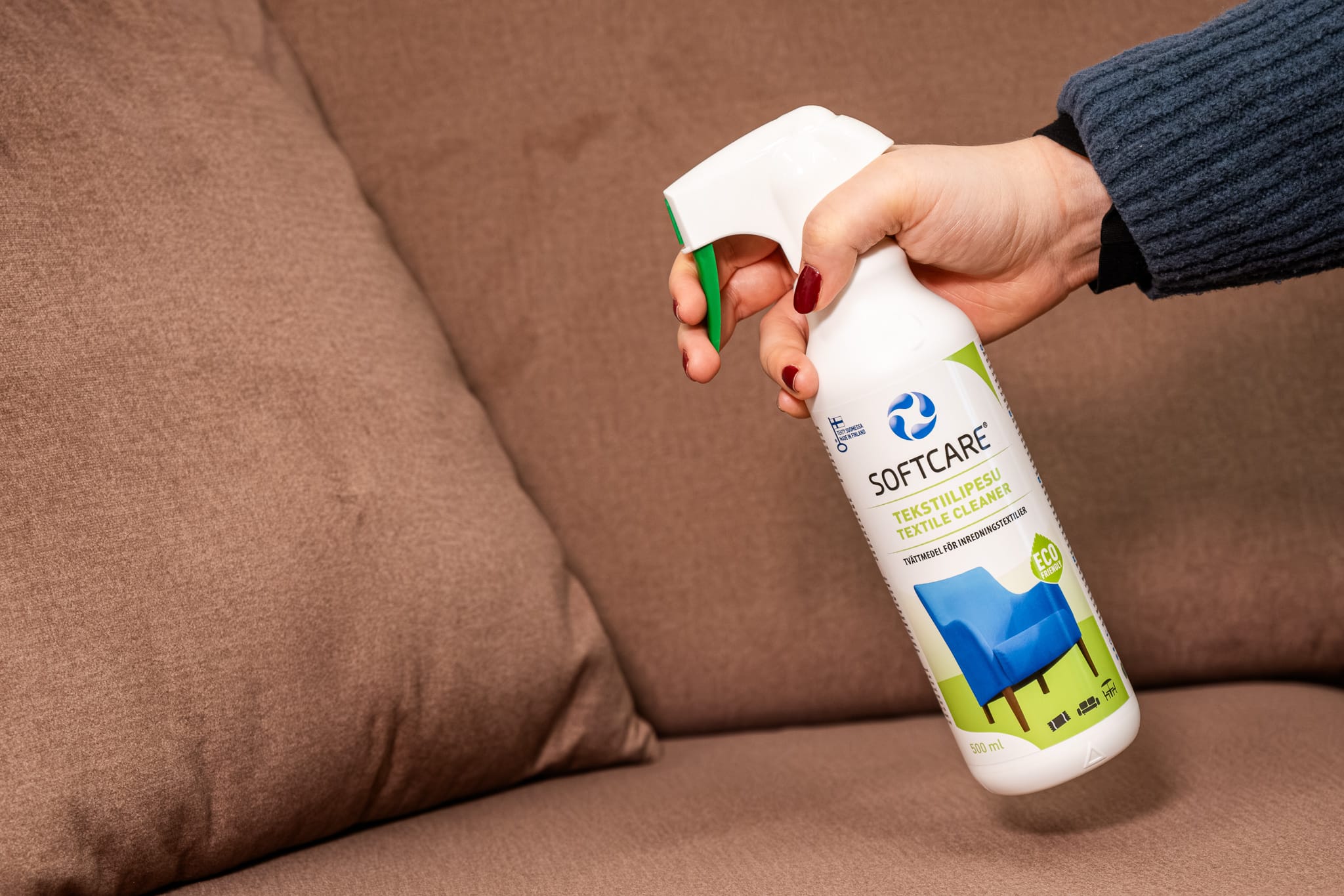 Person holding a textile cleaning product in front of the sofa